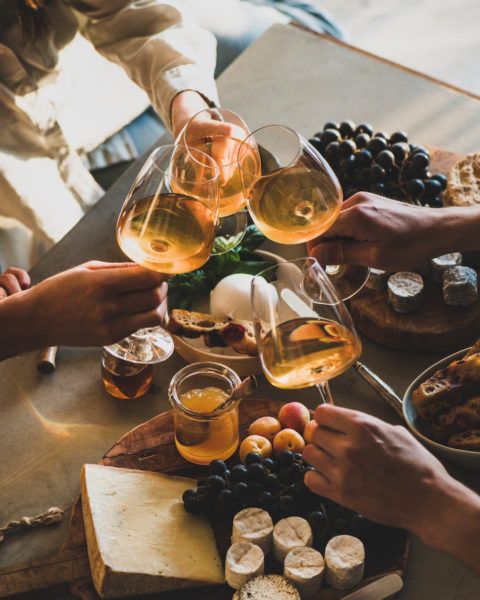 Wein und Käse auf einem Tisch mit Früchten, vier Frauen stoßen mit einem Glas Weißwein miteinander an